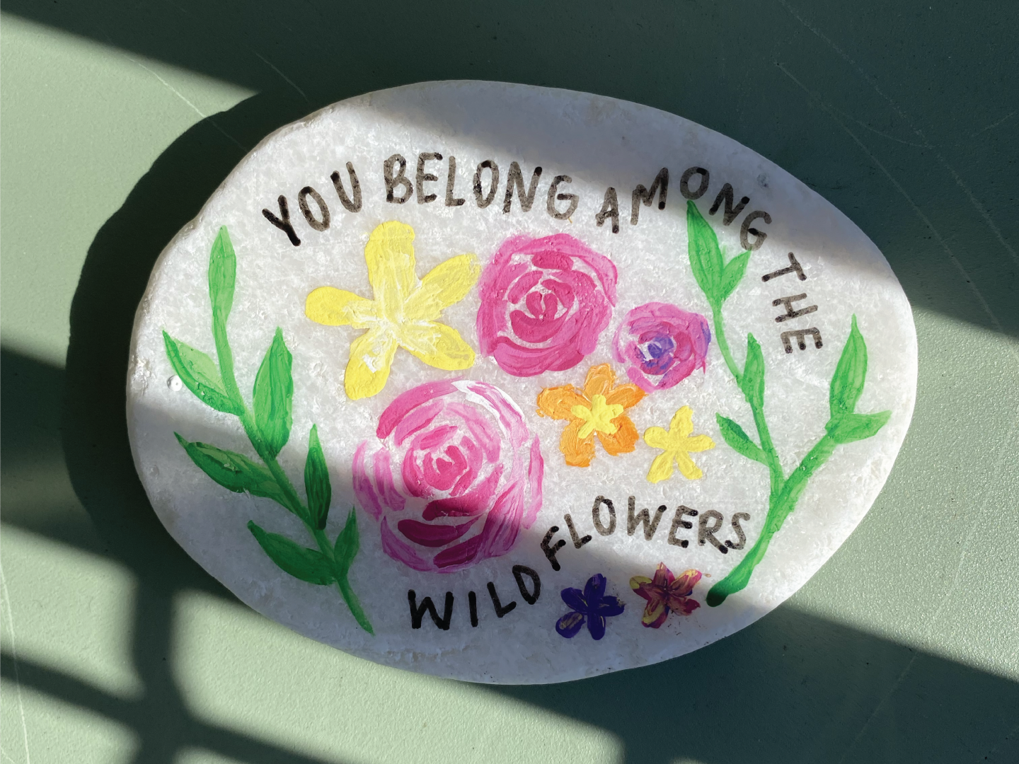 painted rock that says you belong among the wildflowers with painted pattern of leaves and flowers